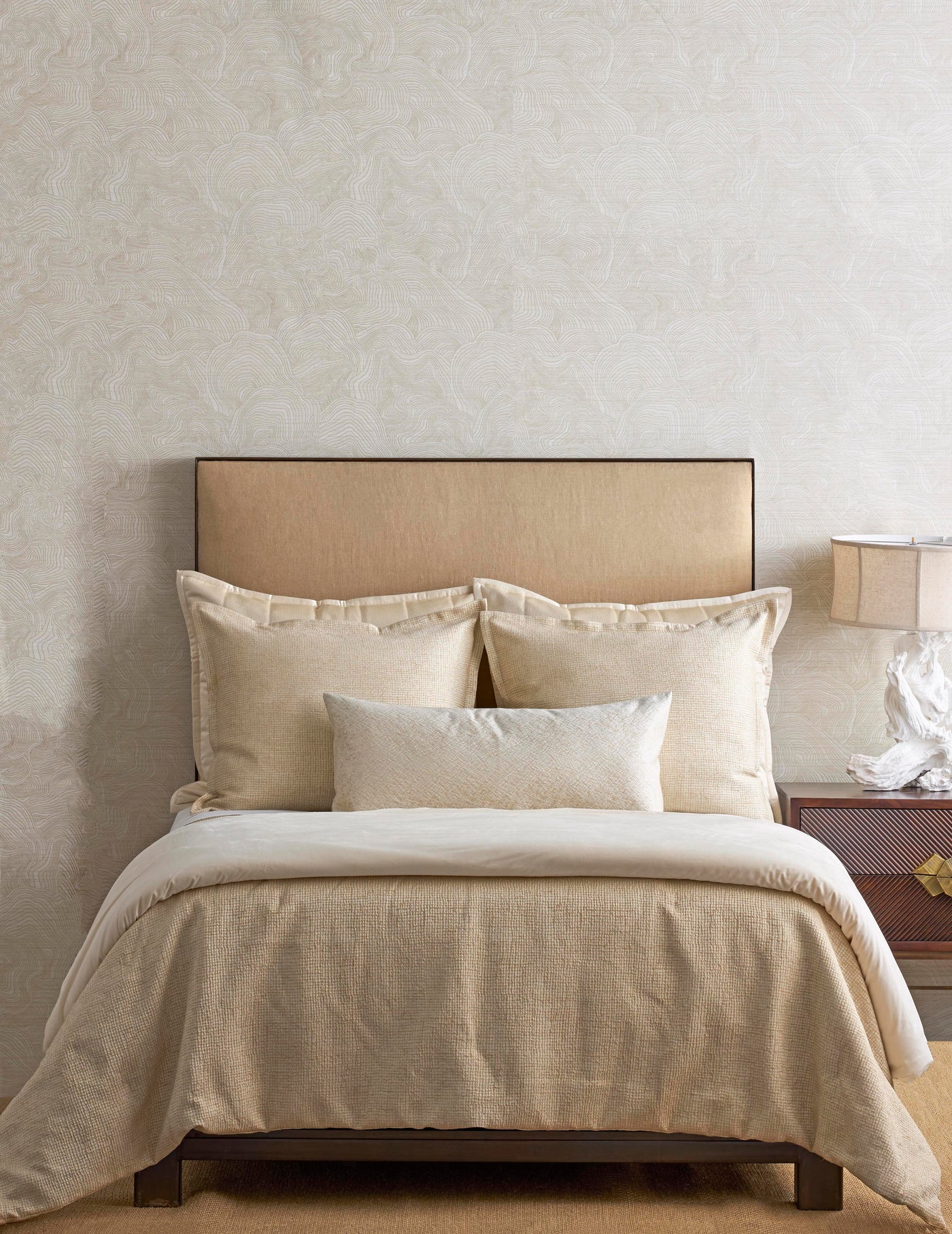 Champagne textured coverlet and pillows styled on a neutral bed against a botanical wallpaper.