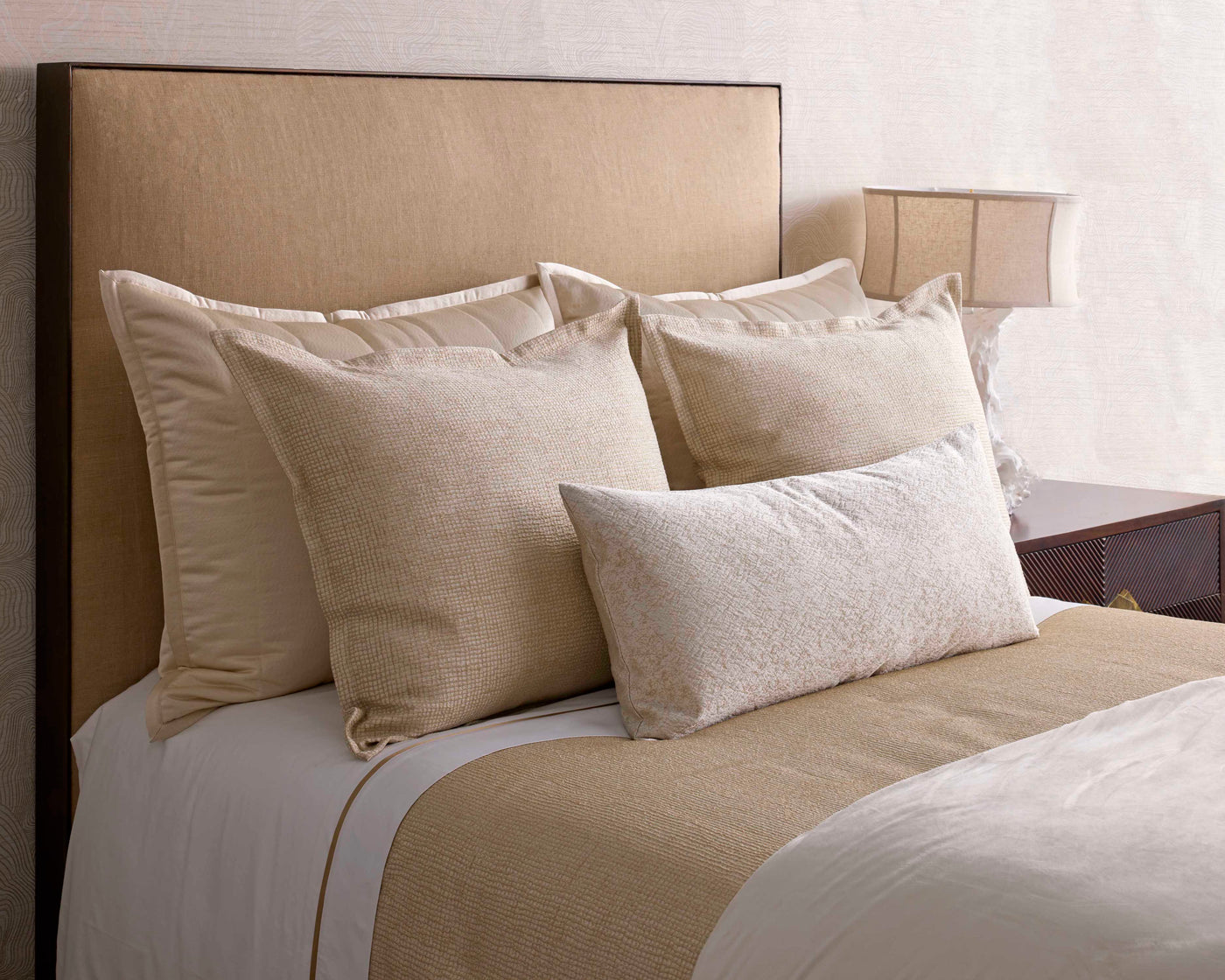 Neutral-toned bed styled with layered champagne and ivory pillows and a textured coverlet.