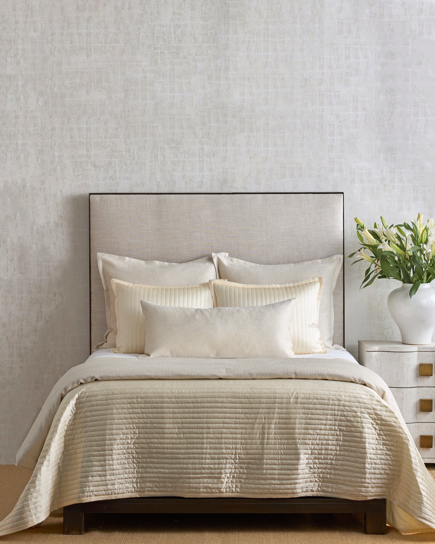 Ivory quilted coverlet draped over a styled bed with layered neutral pillows.