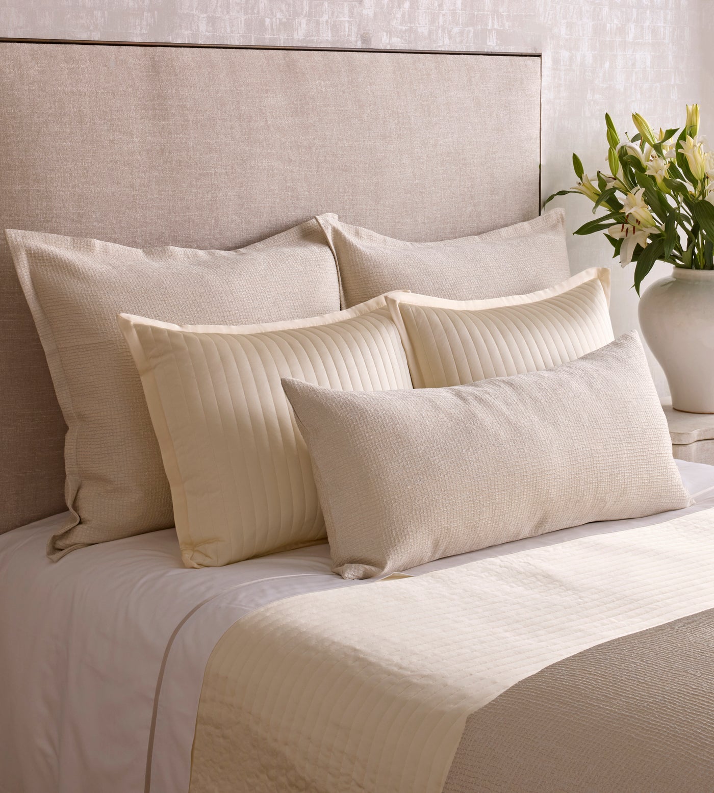 Layered ivory and champagne bedding styled with mixed-texture pillows and white florals.