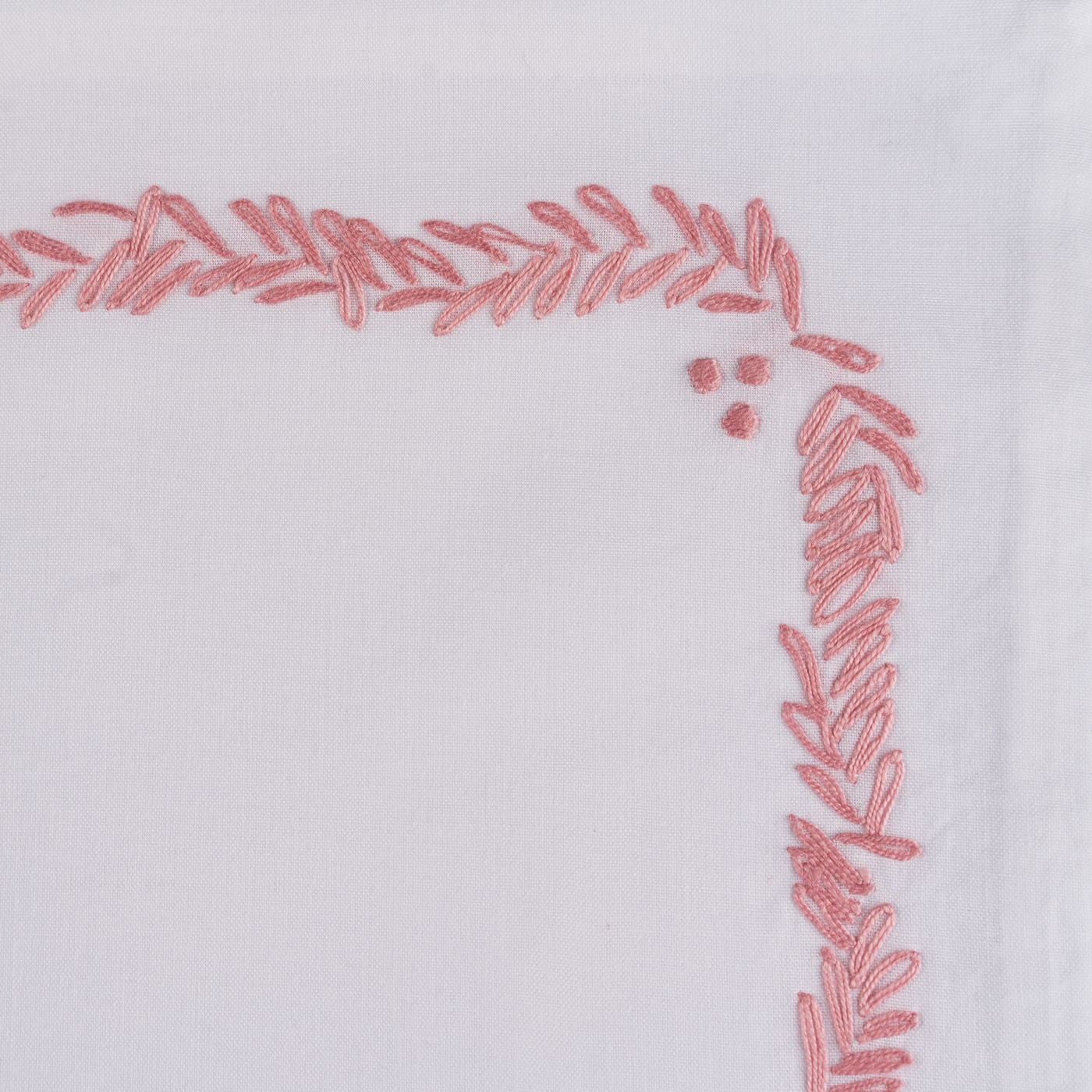 Corner detail of rose embroidered leaf garland border on white linen.