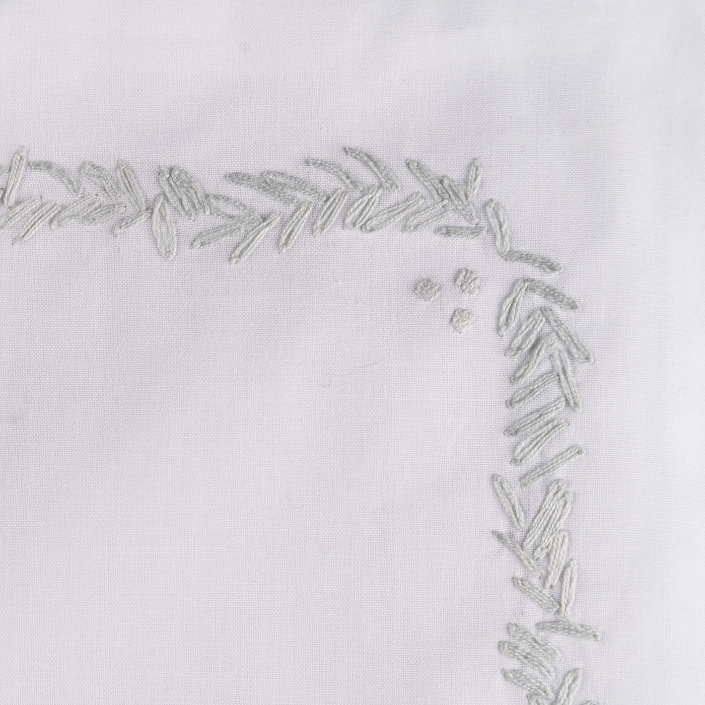 Close-up of silver embroidered leaf border on white linen, corner detail.