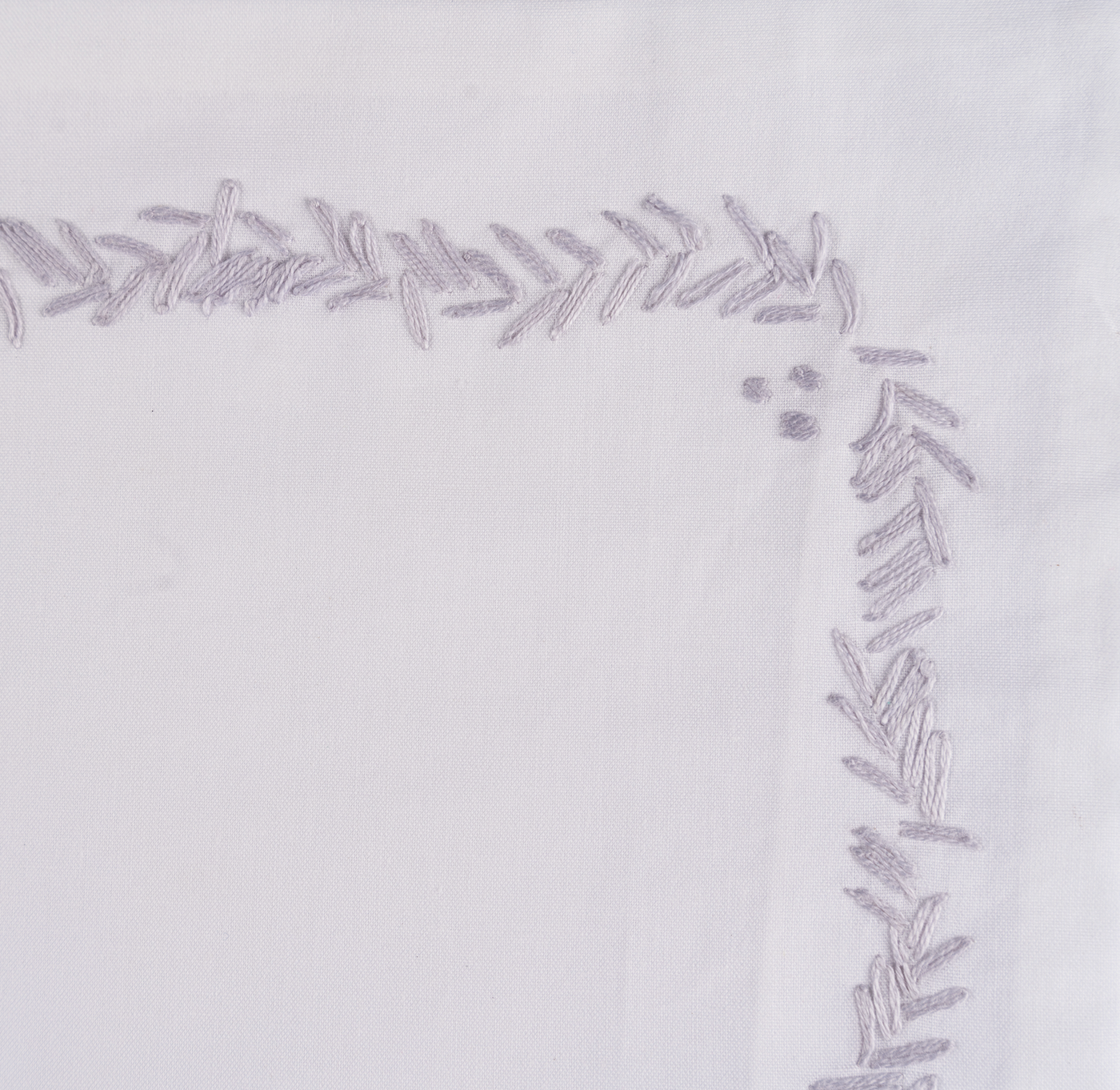 Corner detail of silver leaf embroidery on white cotton sheeting.