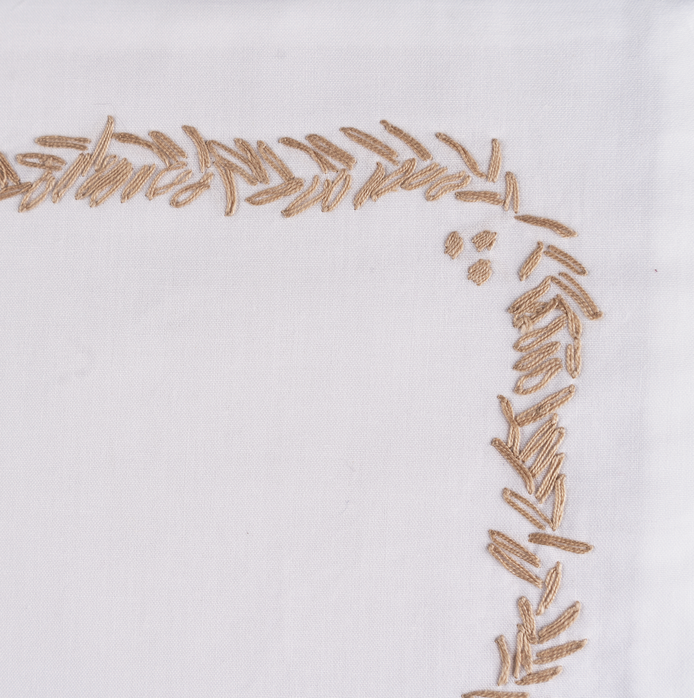Corner detail of gold embroidered leaf border on white cotton sheeting.