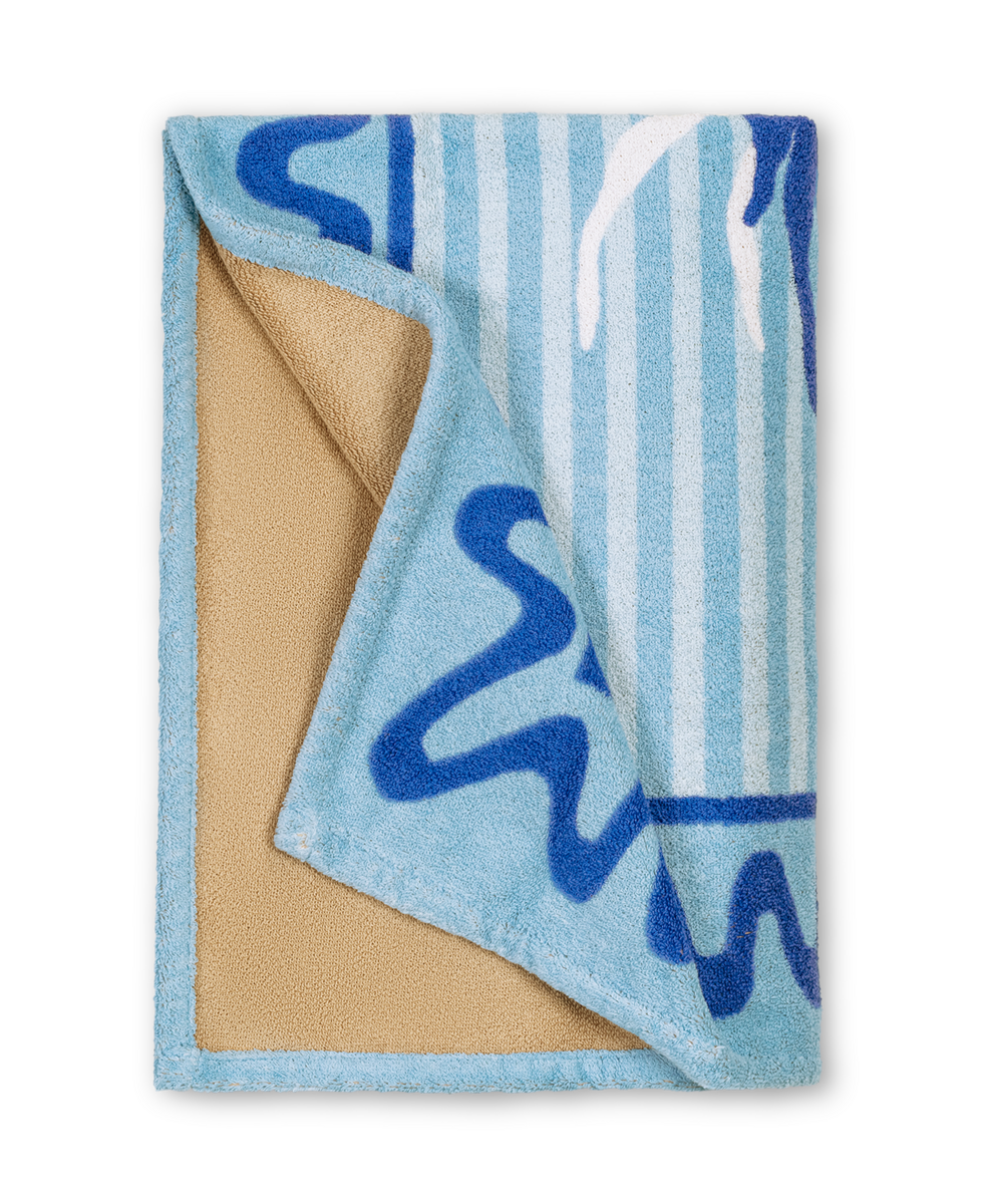 The Matouk Seahorse Beach Towel is a folded, rectangular towel featuring blue and white stripes, abstract blue designs, and a beige underside.