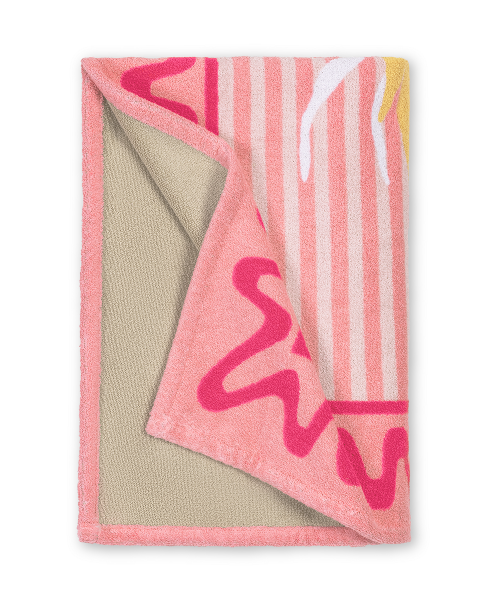 The Matouk Seahorse Beach Towel is pink with abstract patterns and vertical stripes on top, a beige underside, and part of the beach collection.