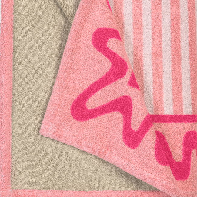 A partially folded Matouk Seahorse Beach Towel in pink, featuring wavy and striped patterns from the beach collection, rests on a beige textured surface.