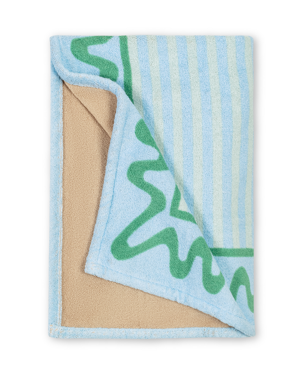 The Seahorse Beach Towel by Matouk features a beige underside and a blue top with green squiggly lines and vertical stripes, from our beach collection.