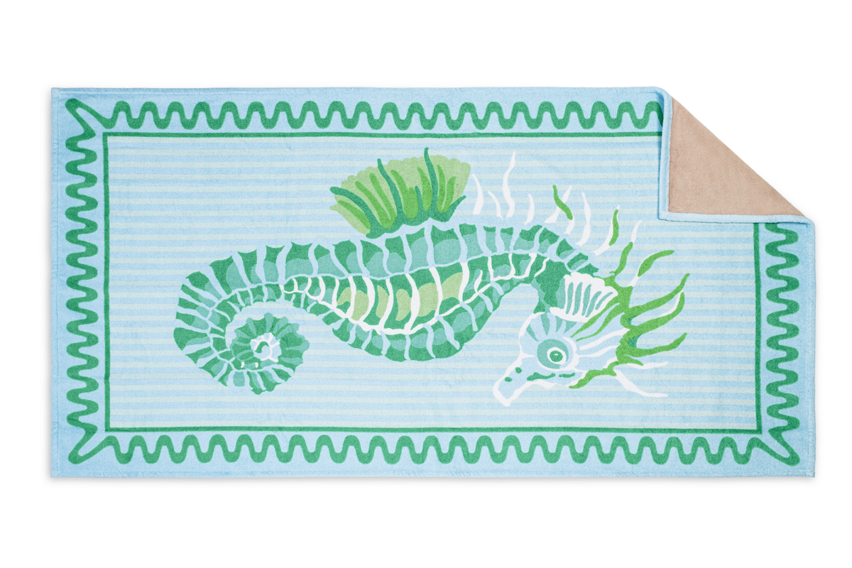 The Matouk Seahorse Beach Towel features a green seahorse on a blue and white striped background with a beige corner fold, part of our exclusive beach collection.