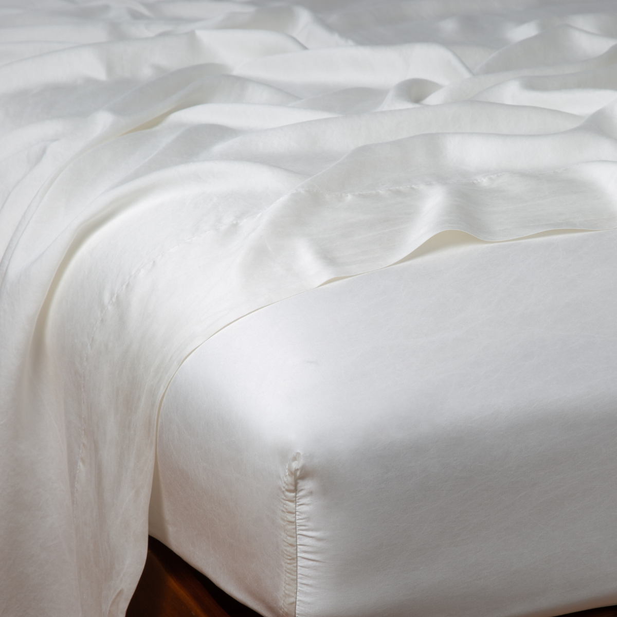Close-up of Bella Notte Seraphina fitted sheet corner in Winter White with draped fabric above.