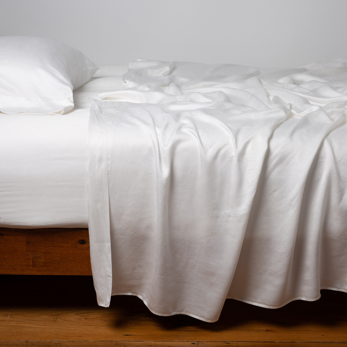 Bella Notte Seraphina flat sheet in White, draped loosely over a wood-frame bed.