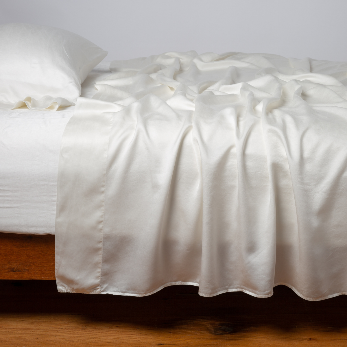 Bella Notte Seraphina flat sheet in Winter White draped over bed, showing lustrous satin fabric.