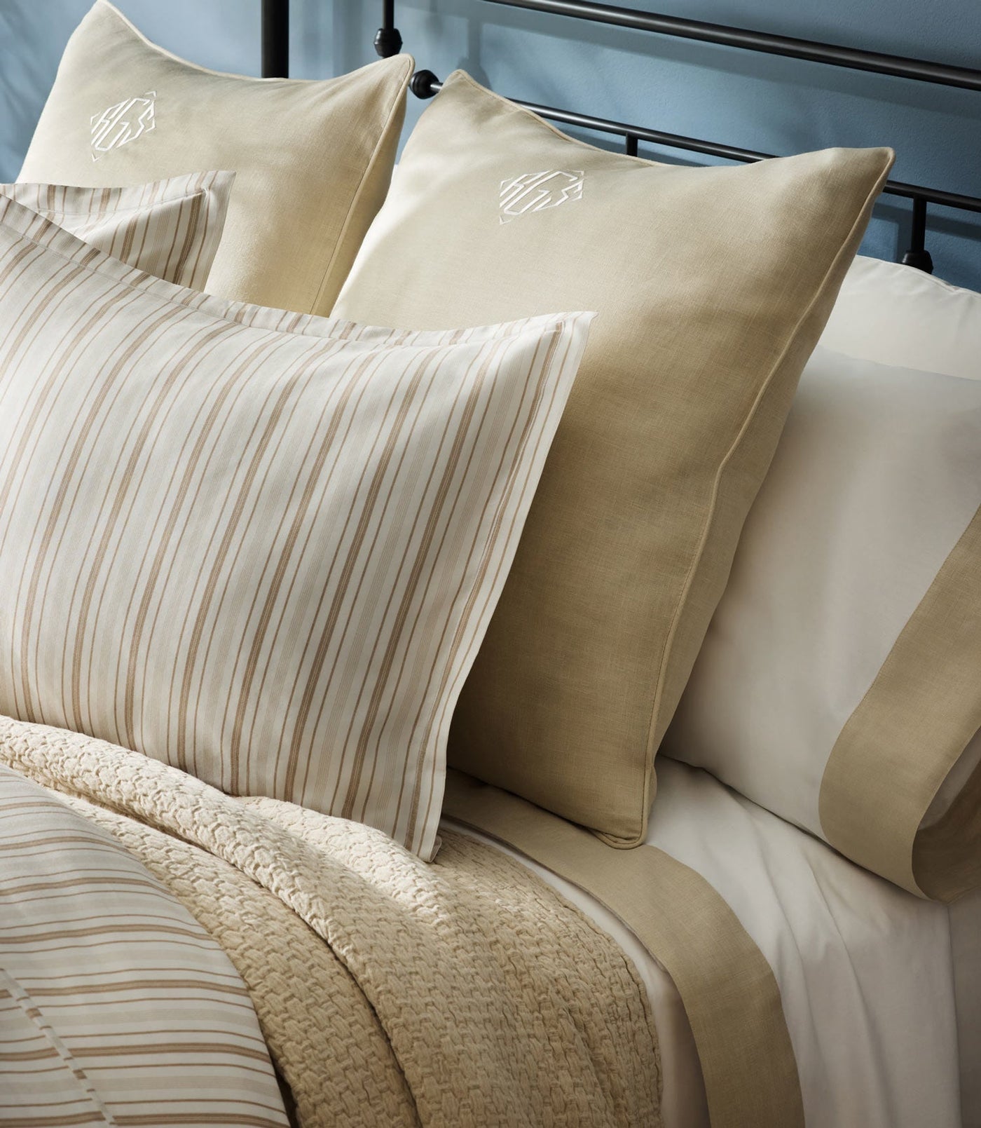 Close-up of champagne striped pillow layered with ivory euro shams on styled bed.