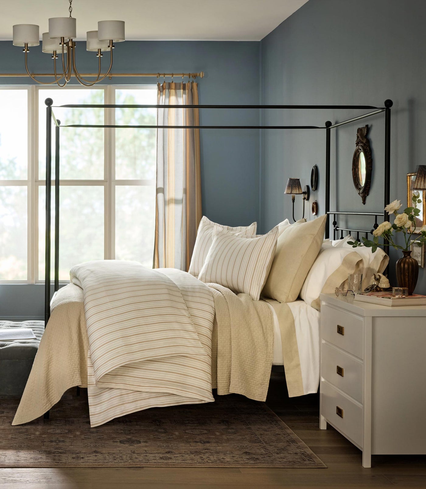 Ivory striped duvet cover styled on iron canopy bed in blue room.