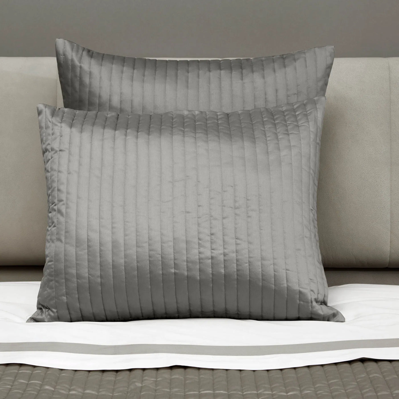 Two gray textured pillows on a bed with a neutral background