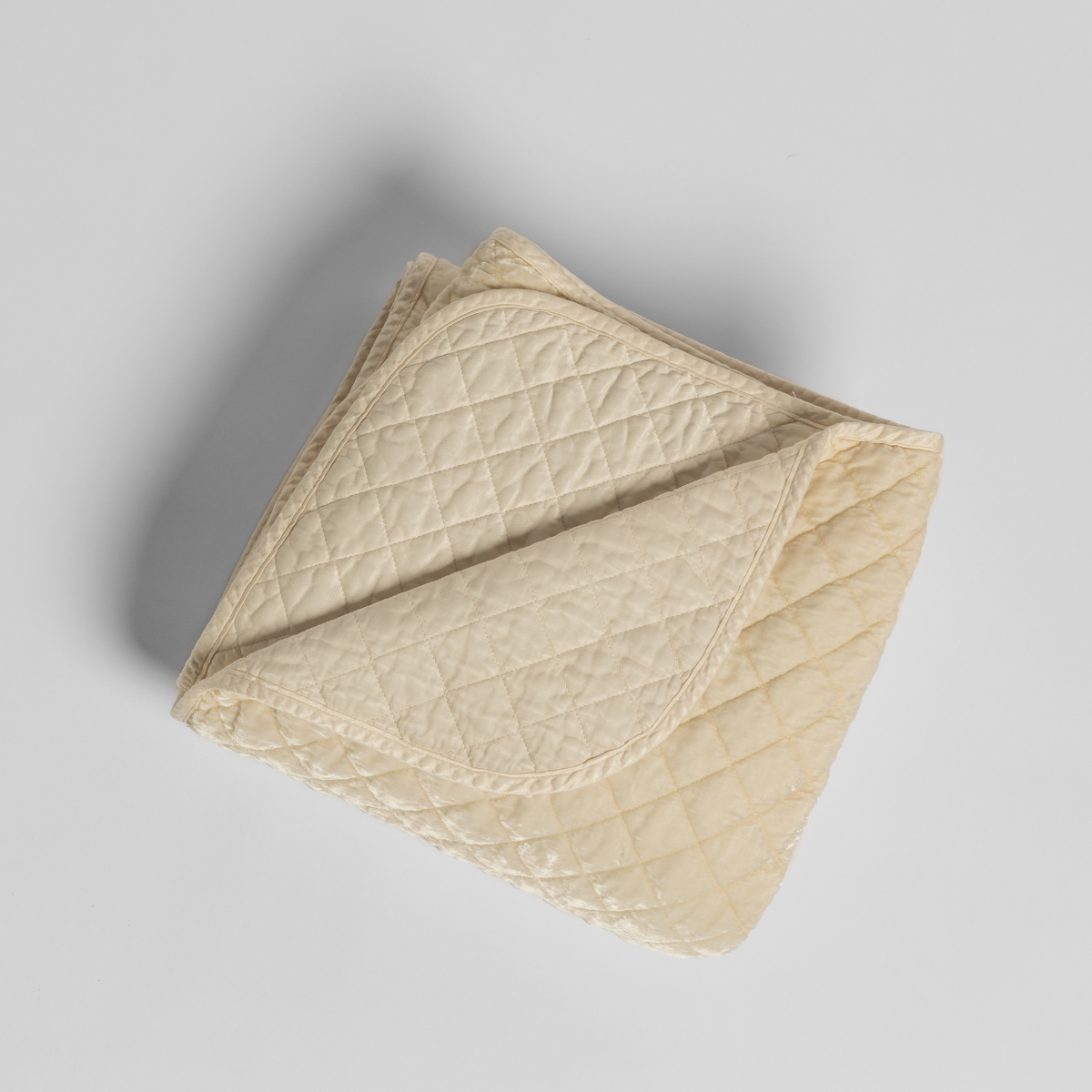 Bella Notte Silk Velvet quilted blanket in Crema, folded to show diamond quilting and trim detail.