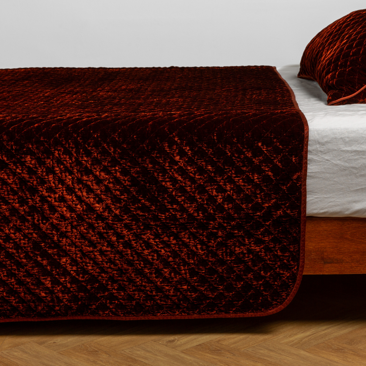 Autumn Silk Velvet quilted coverlet draped over a wood-frame bed, rich diamond quilt pattern.
