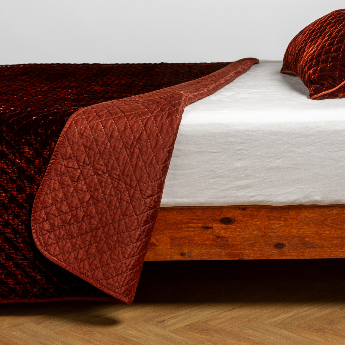 Bella Notte Silk Velvet Quilted Coverlet in Autumn draped over foot of wood bed frame.