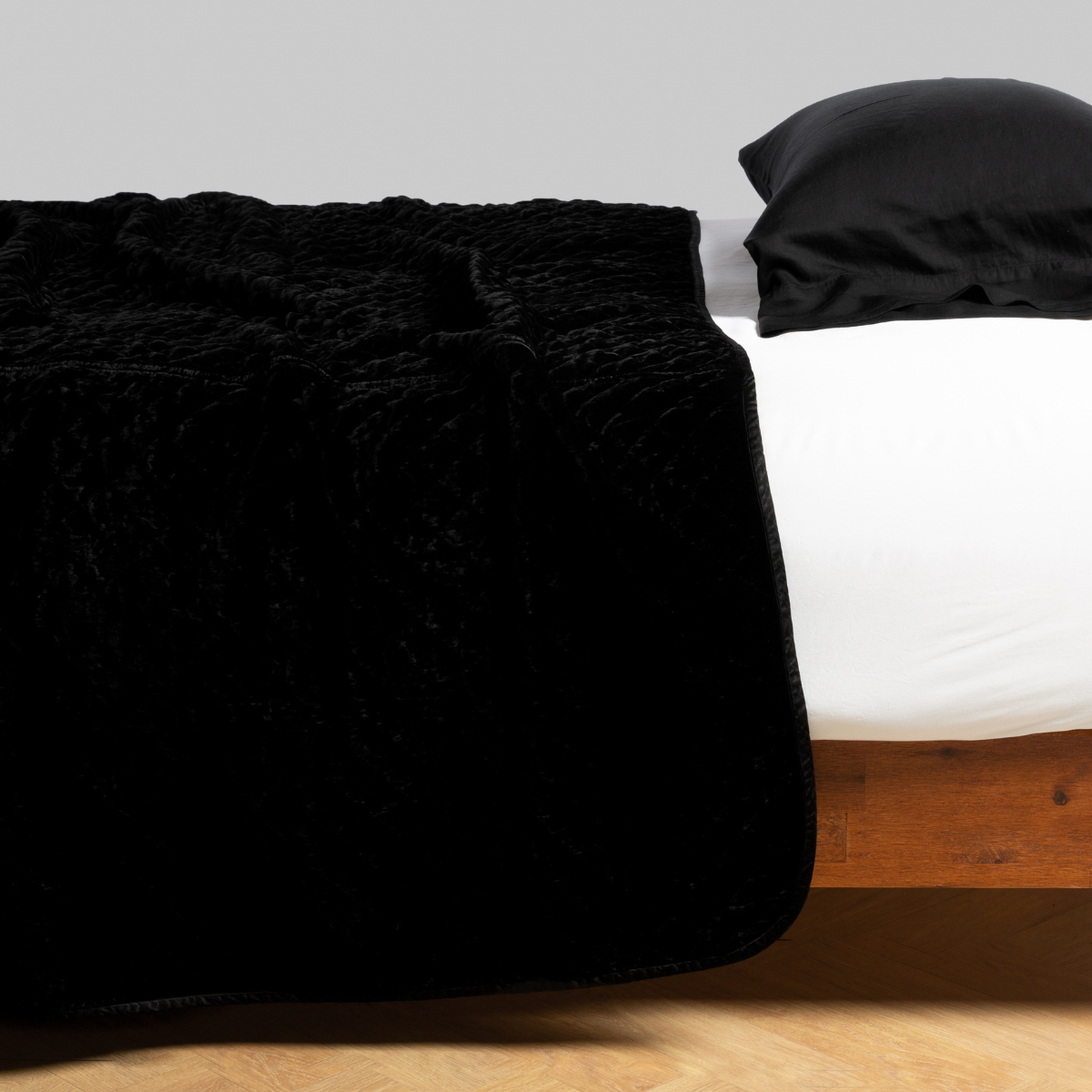 Bella Notte Silk Velvet Quilted Coverlet in Corvino draped over foot of bed, angled view.