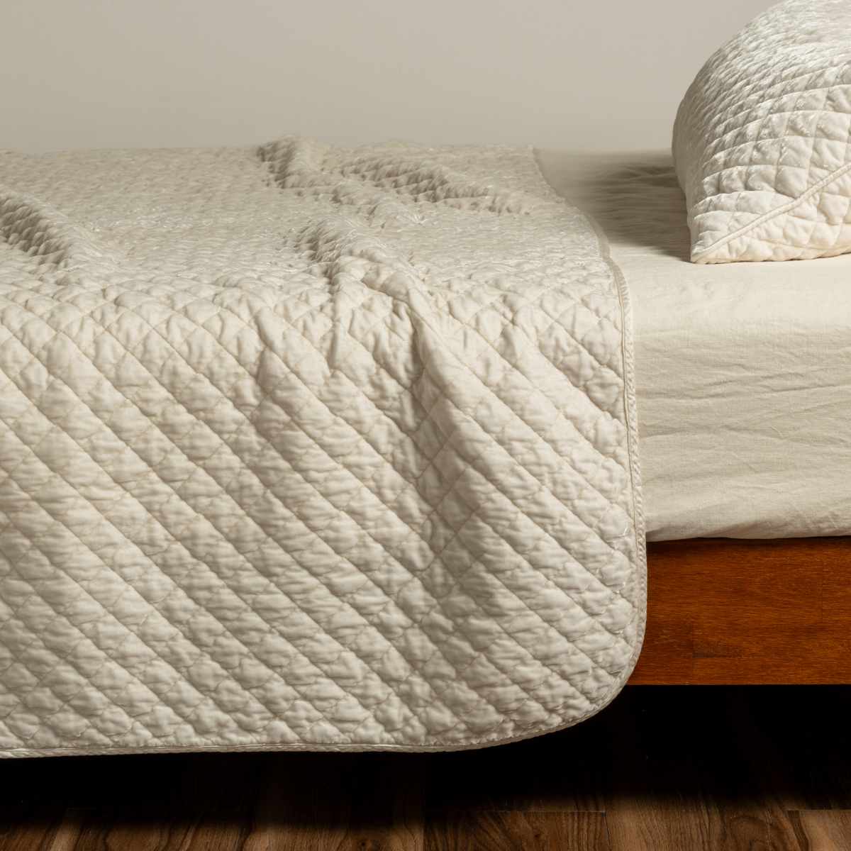 Bella Notte Silk Velvet coverlet in Crema, showing corner drape over wooden bed frame.