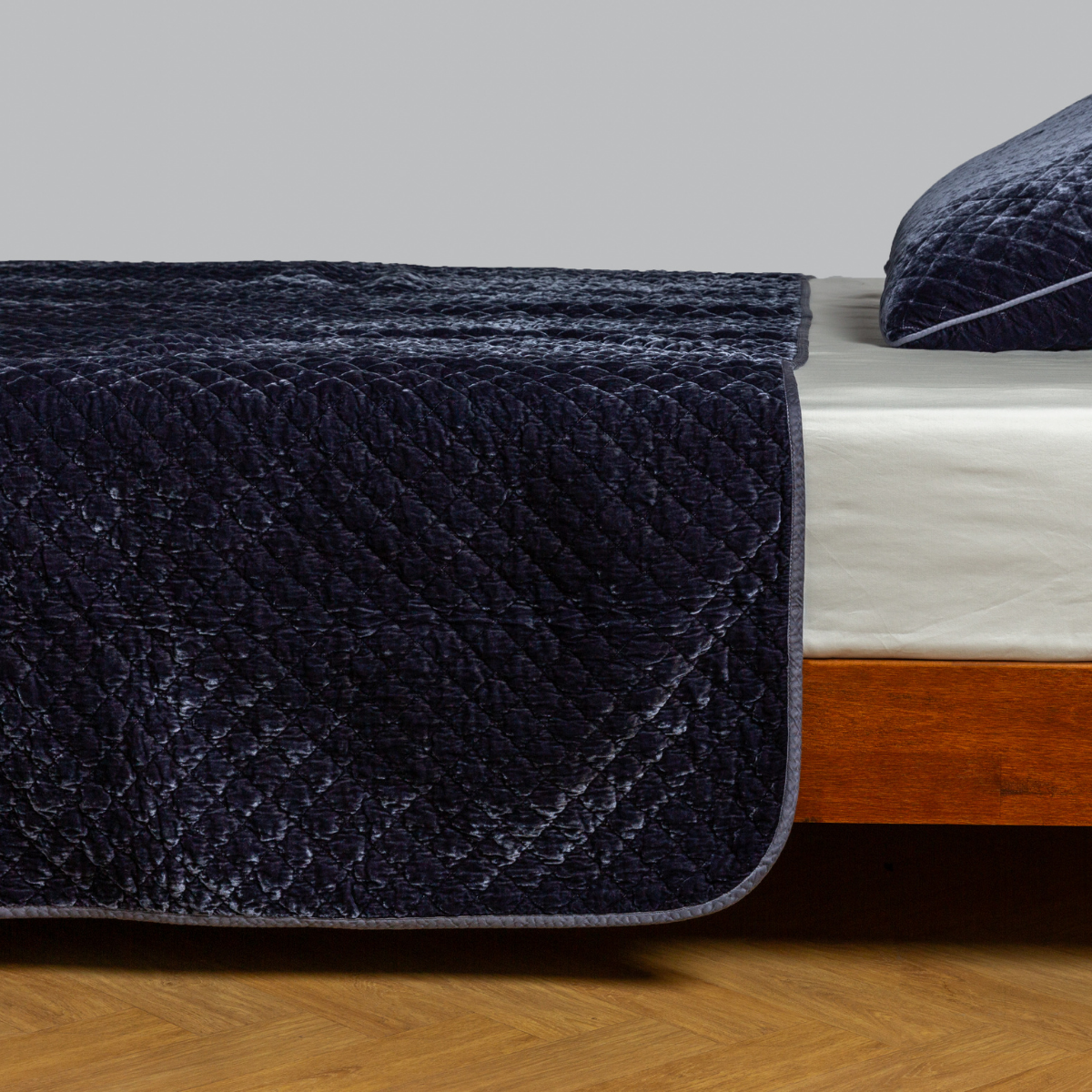Bella Notte Silk Velvet Quilted Coverlet in French Lavender draped over foot of wood bed.