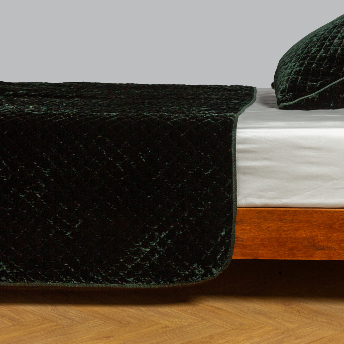 Deep Juniper quilted silk velvet coverlet draped over bed foot, diamond pattern visible.
