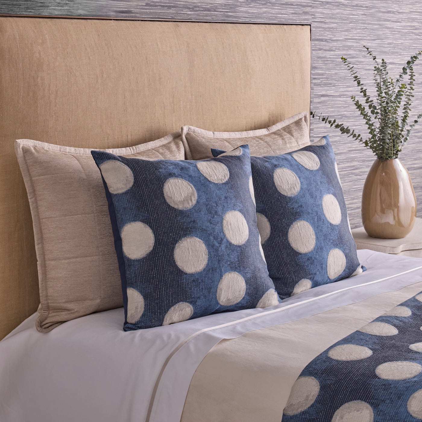 Close-up of blue and ivory polka dot pillows styled on a made bed with neutral bedding.