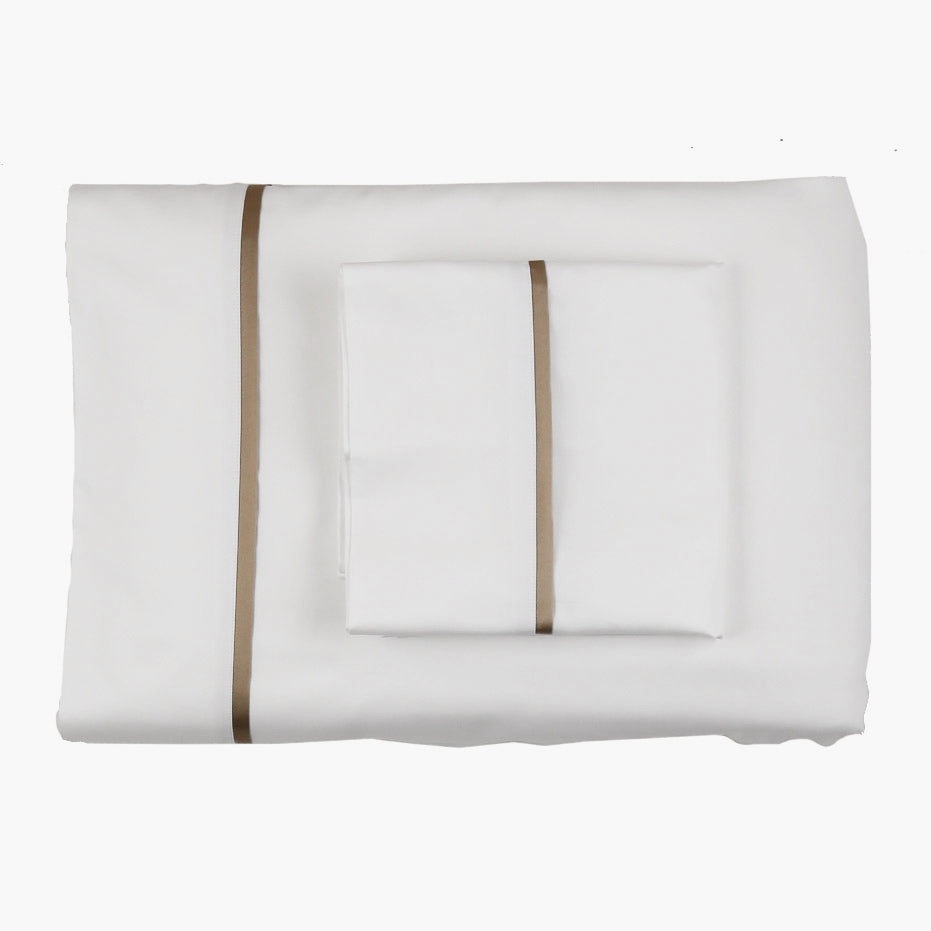 Close-up overhead view of white silk sheet set with single taupe trim stripe, neatly folded.