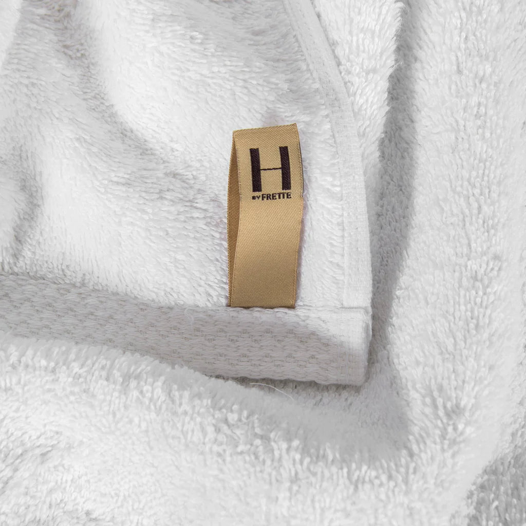 The Simple Border Bath Sheet Set by Frette is a white terry cloth luxury towel set featuring a beige fabric tag with an H and “by FRETTE,” crafted from premium 100% cotton for those who value quality.