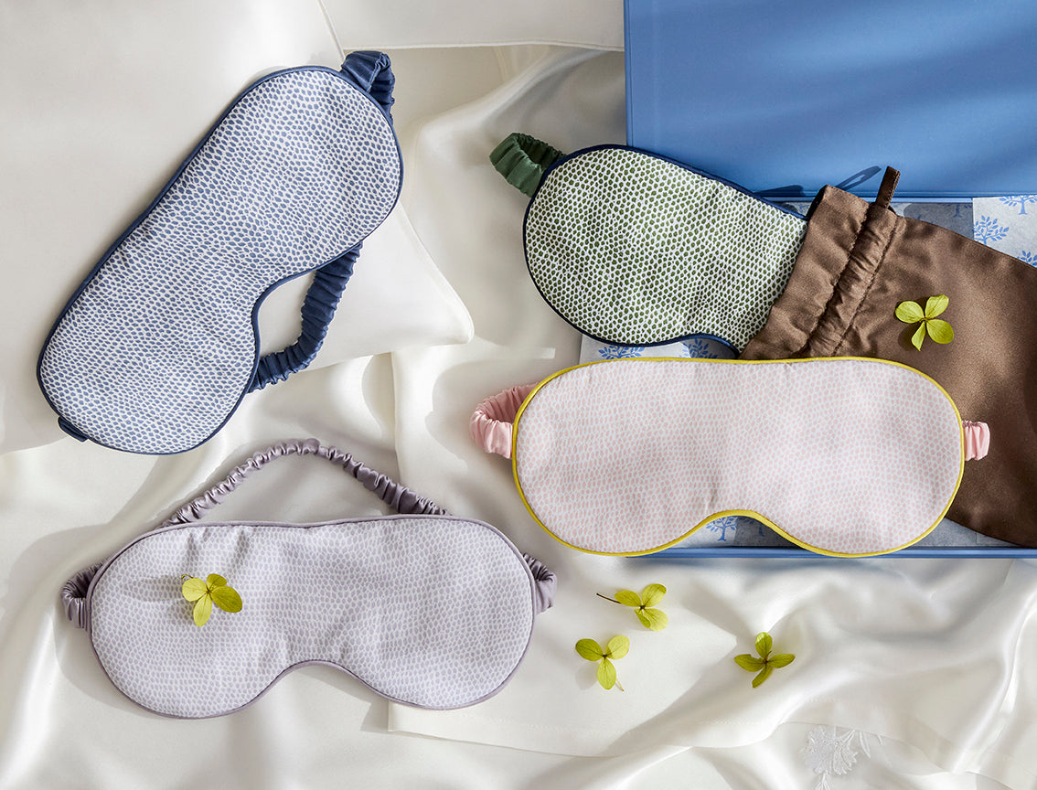 Matouk Jasper sleep masks in blue, sage, lavender, and ivory with yellow trim.