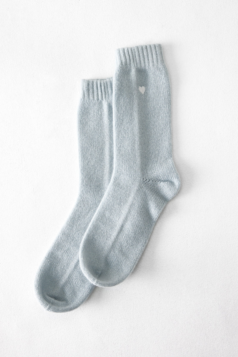 The Matouk Sleeping Socks by Matouk are light blue, cozy socks featuring a small white heart near the top, displayed flat on a white surface.