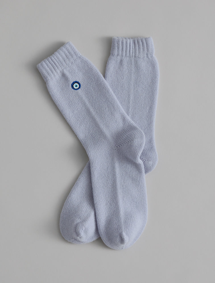 The Matouk Sleeping Socks by Matouk are cozy light gray socks with ribbed cuffs and a blue and white circular emblem near the top, made in Scotland, shown on a plain background.