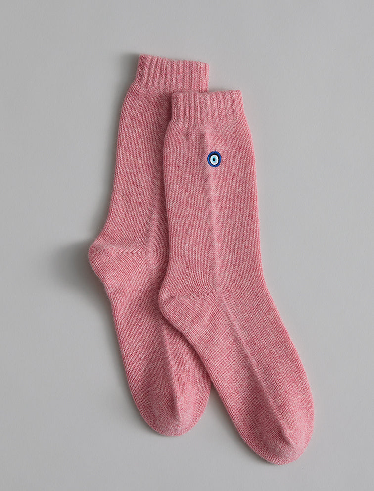 The Matouk Sleeping Socks by Matouk are cozy pink knit socks featuring a small blue and white circular emblem near the top, made in Scotland and displayed on a plain gray background.