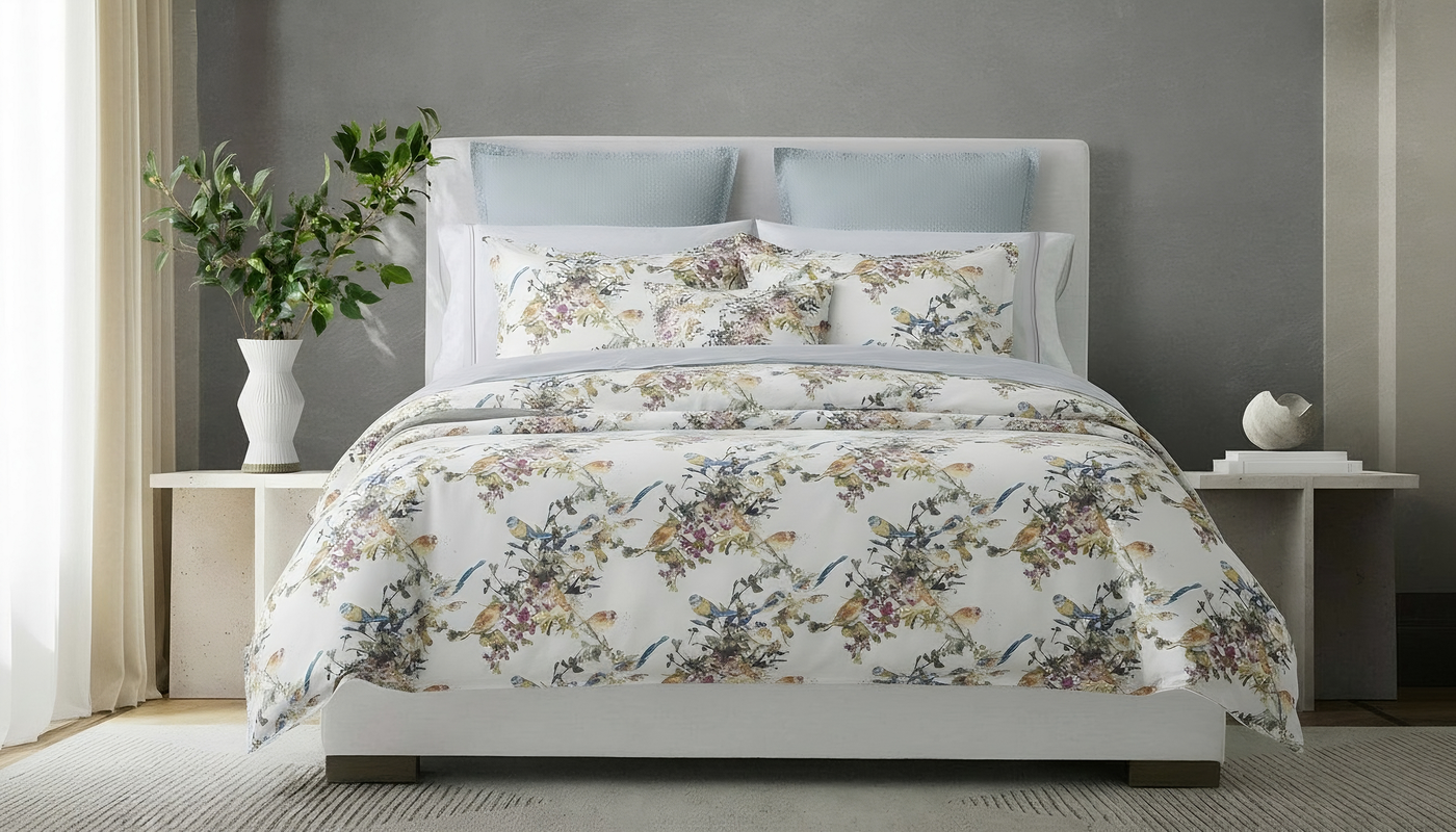 Floral bedding set on a bed in a bedroom setting with a plant and nightstands.