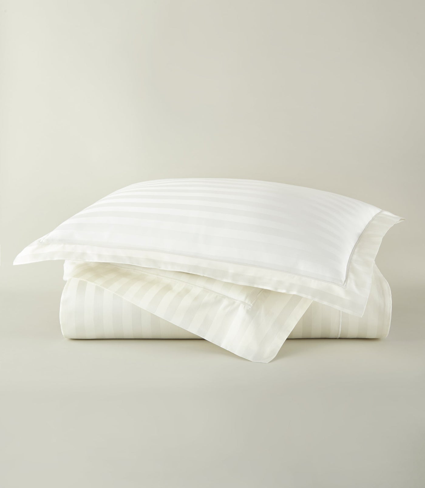 Folded ivory cotton duvet cover with tonal satin stripes, topped with a matching pillowcase.