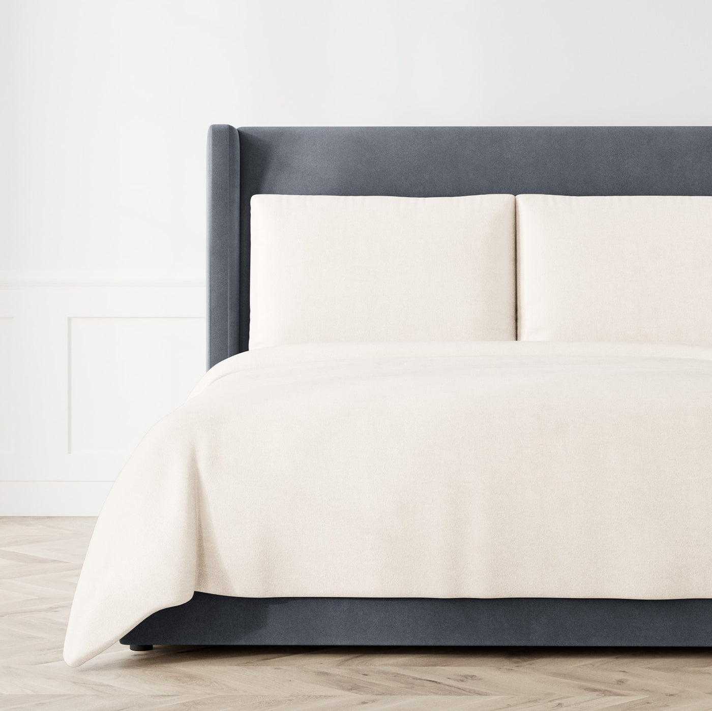 Ivory Ann Gish Stardust coverlet draped over bed with matching shams, styled on charcoal upholstered bed.