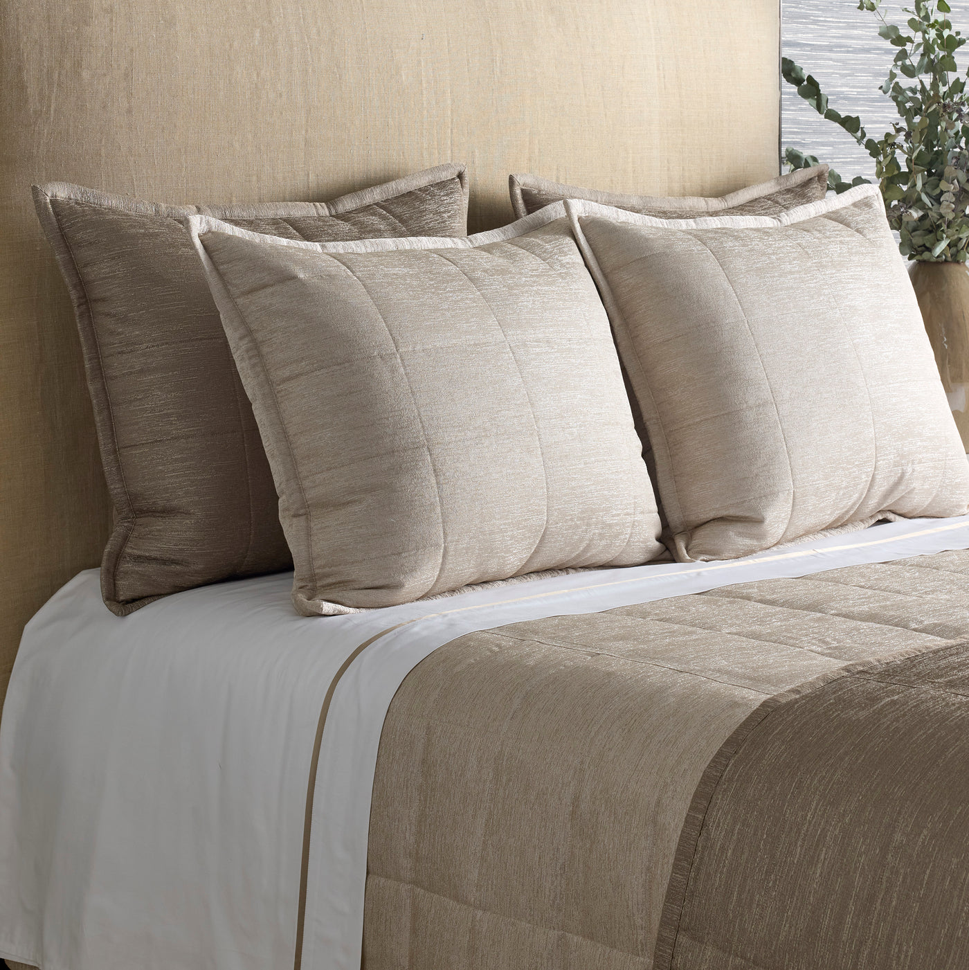 Styled bed with Ann Gish Stria coverlet and shams in warm taupe, showing quilted texture detail.