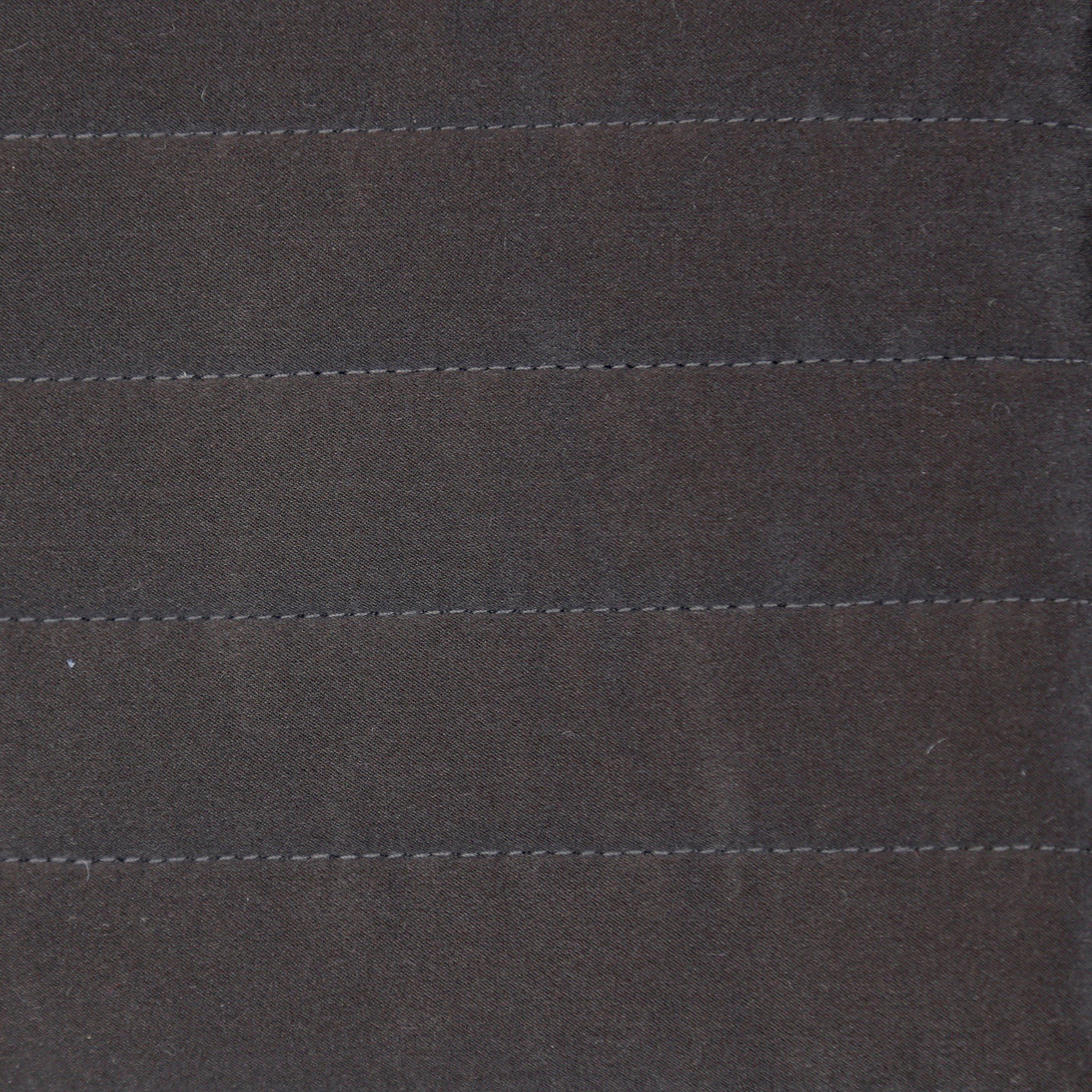 Close-up of charcoal charmeuse fabric with horizontal channel quilting stitches.