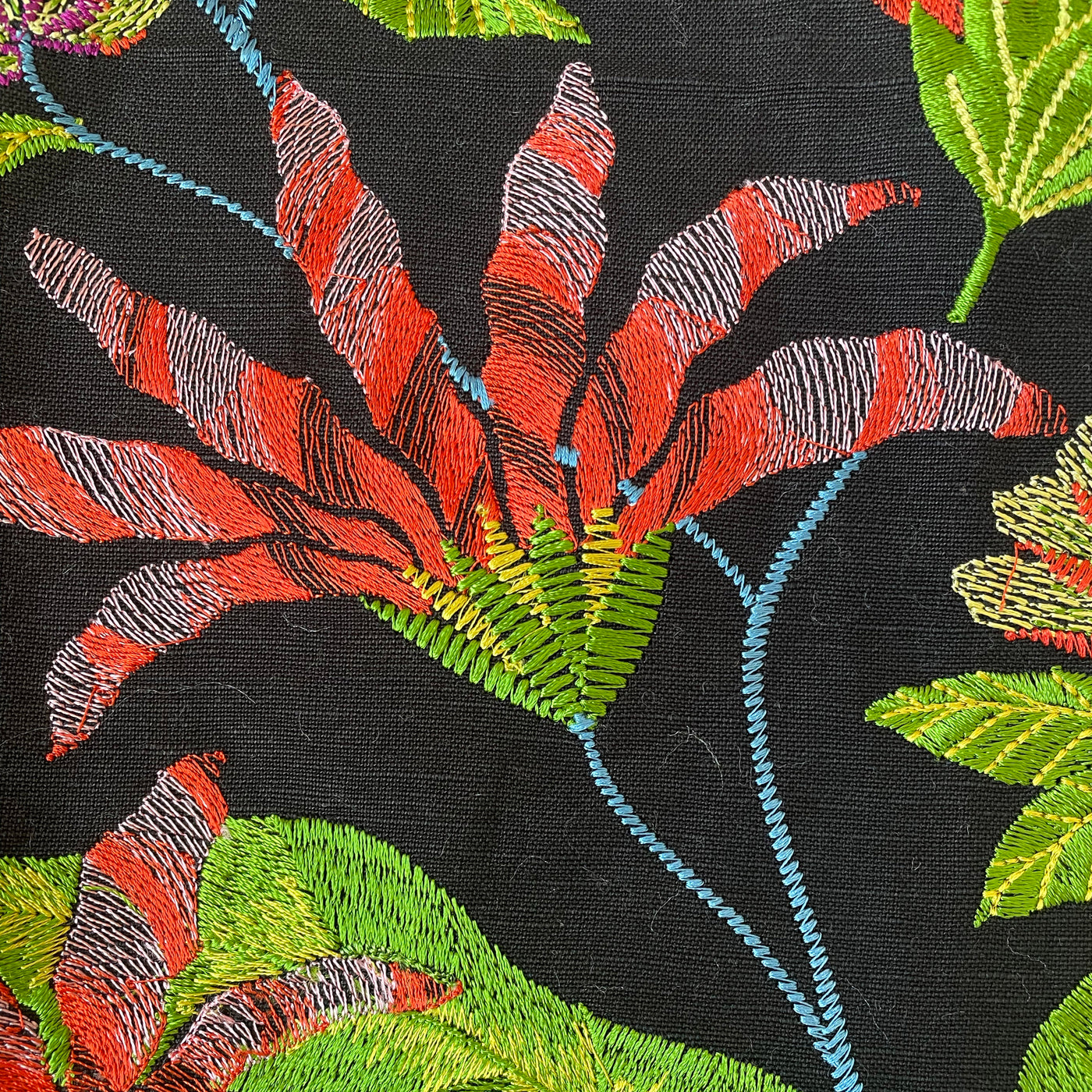 Close-up of red and green floral embroidery on black linen fabric, Ann Gish Forest duvet.