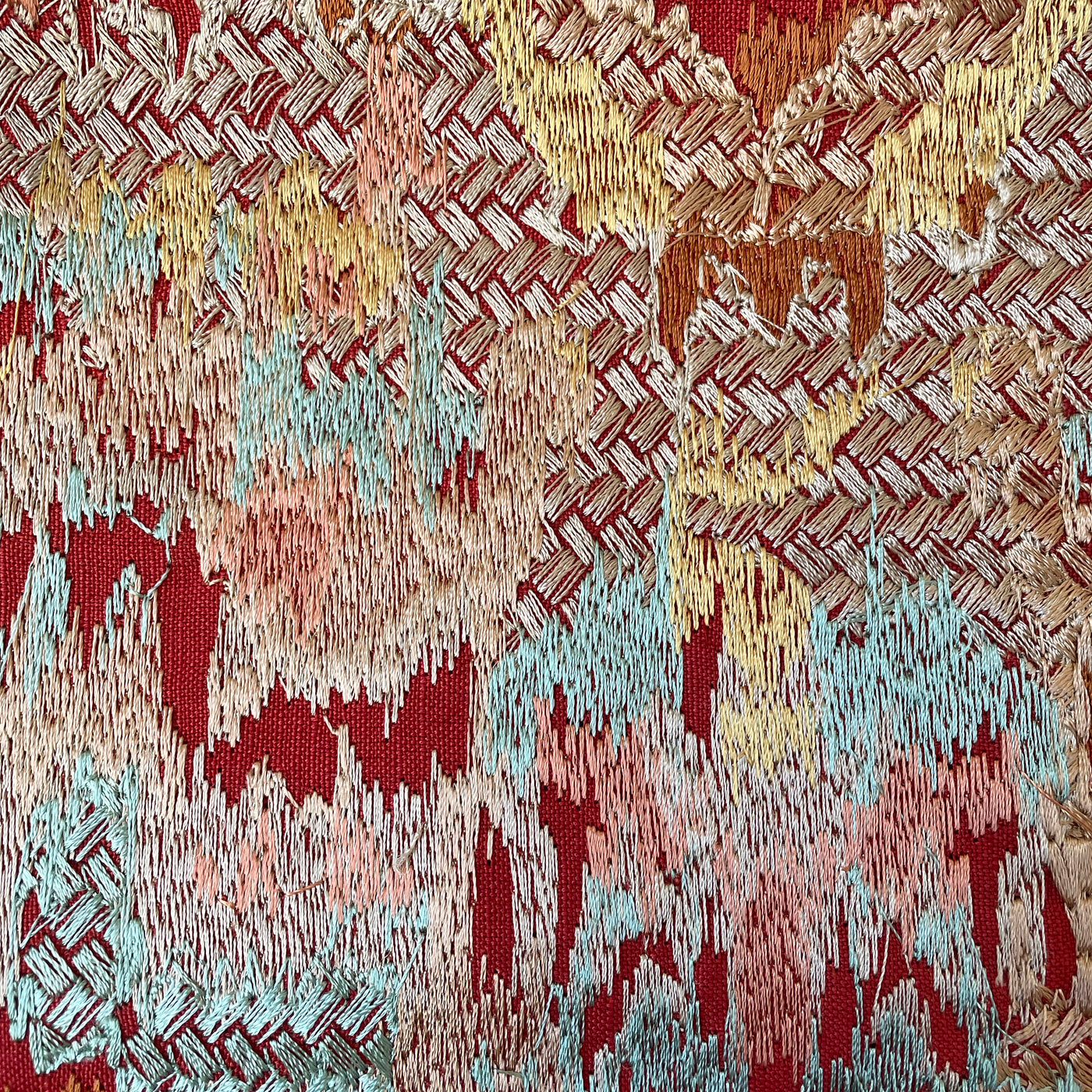 Close-up of Ann Gish Dowry pillow fabric in crimson with aqua, gold, and blush ikat weave detail.