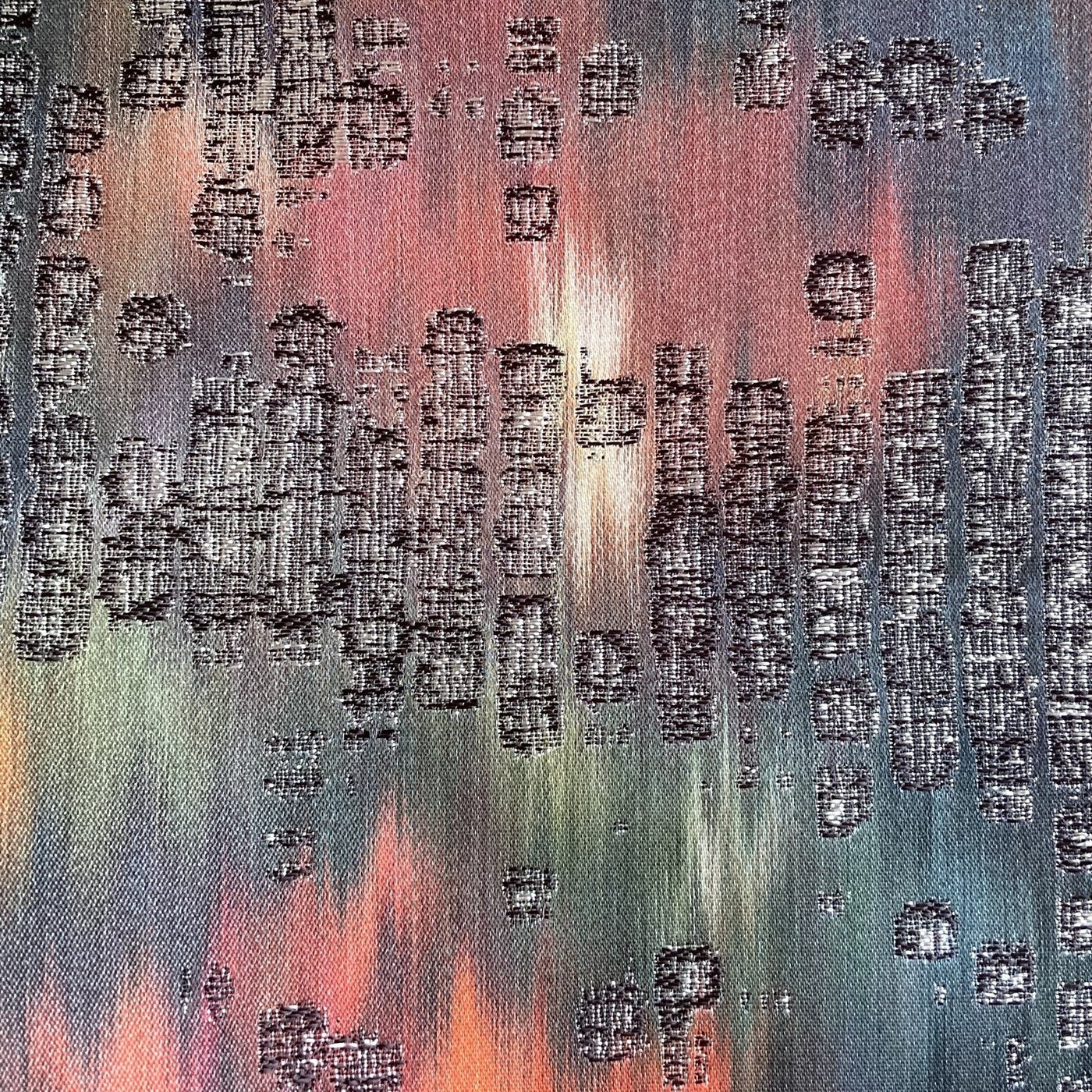 Close-up of Ann Gish Ibiza pillow fabric showing raised woven motifs on multicolor sunset-toned ground.
