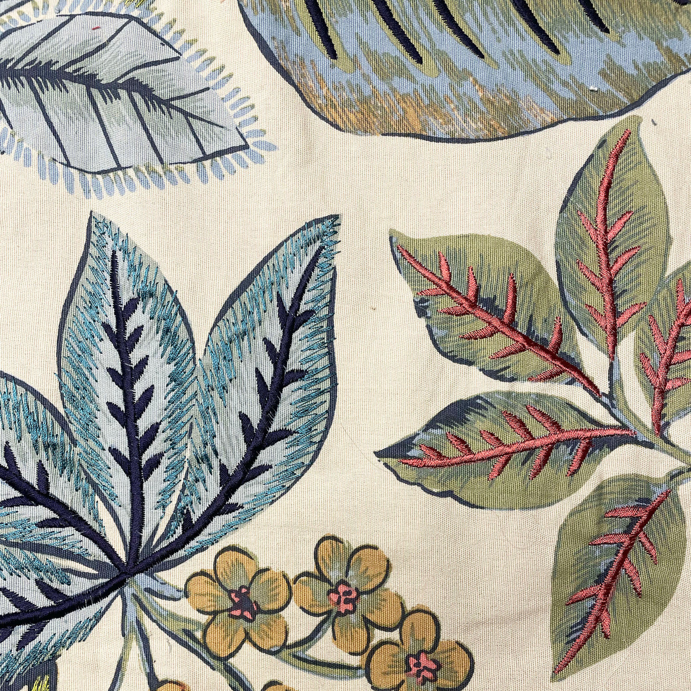 Close-up of Ann Gish Lanai pillow embroidery: teal, green, and red botanical leaves on ivory.