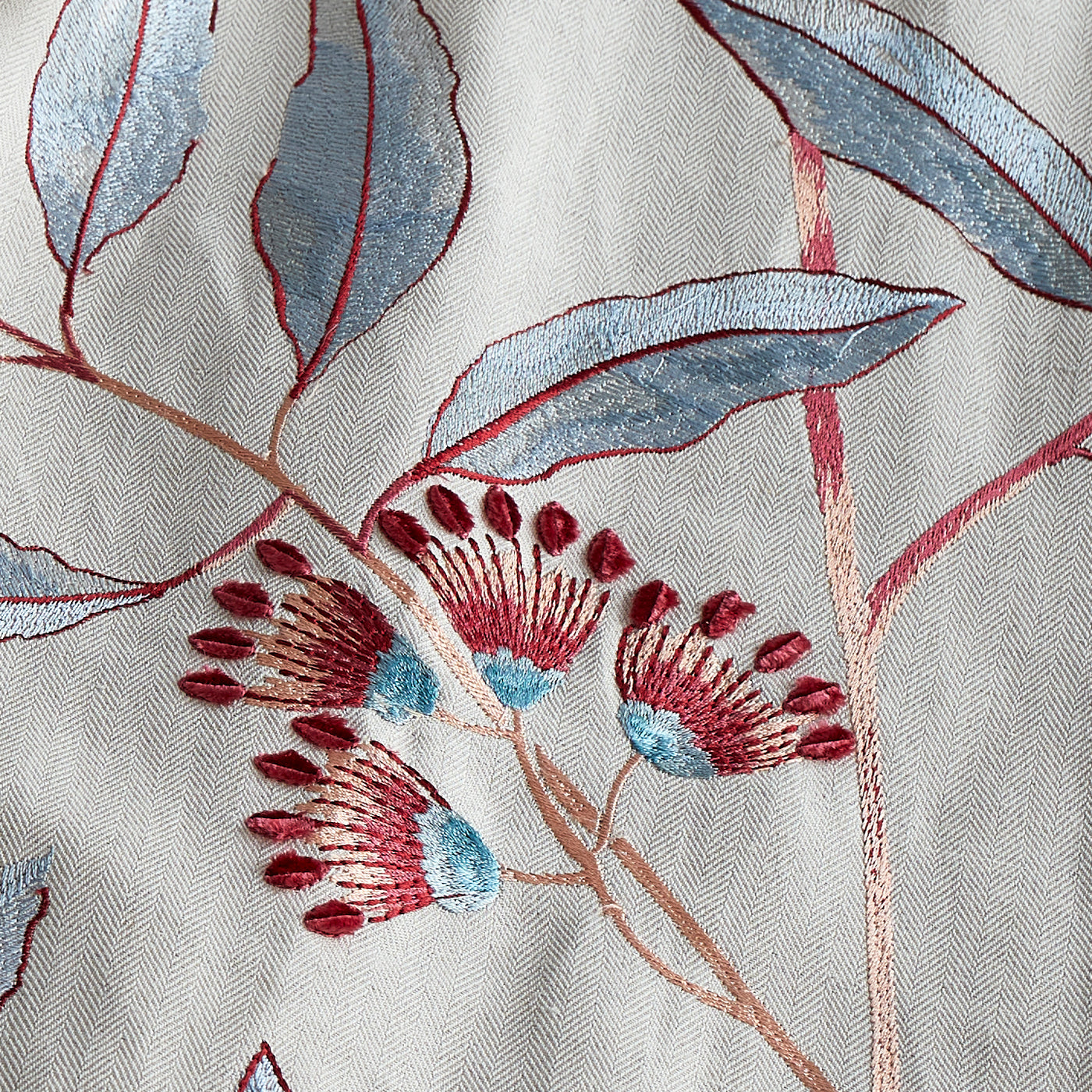 Close-up of Ann Gish Linenberry pillow embroidery: crimson and sky blue floral motifs on silver linen.