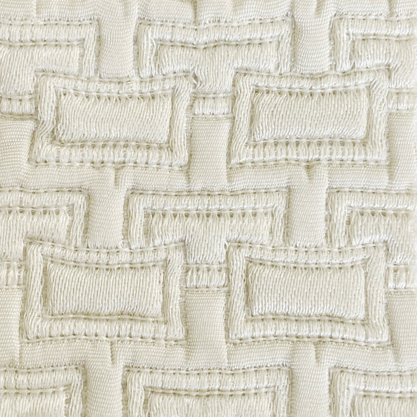 Close-up of ivory woven fabric with raised rectangular geometric embroidery pattern.