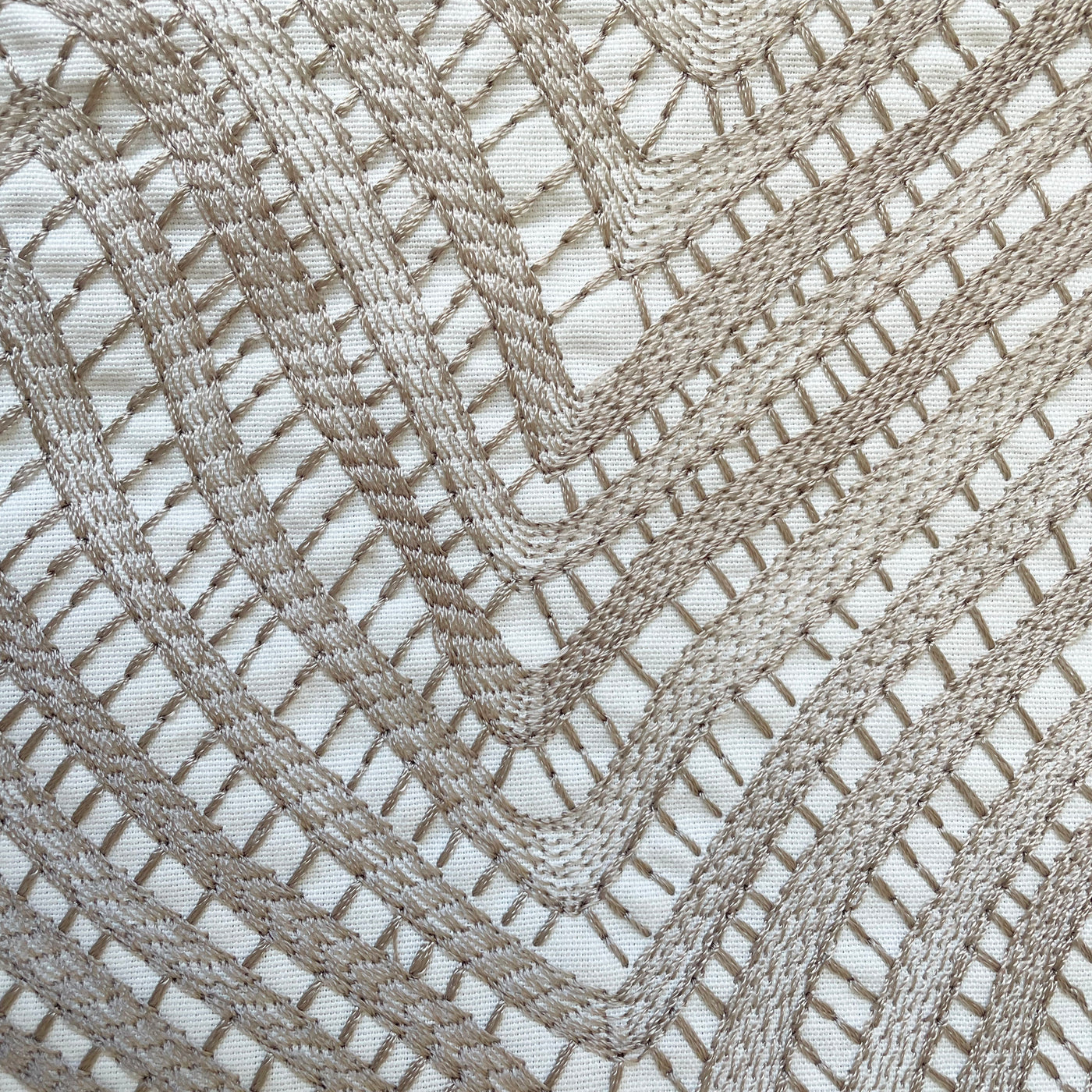 Close-up of taupe geometric crochet lace pattern on ivory fabric pillow cover.