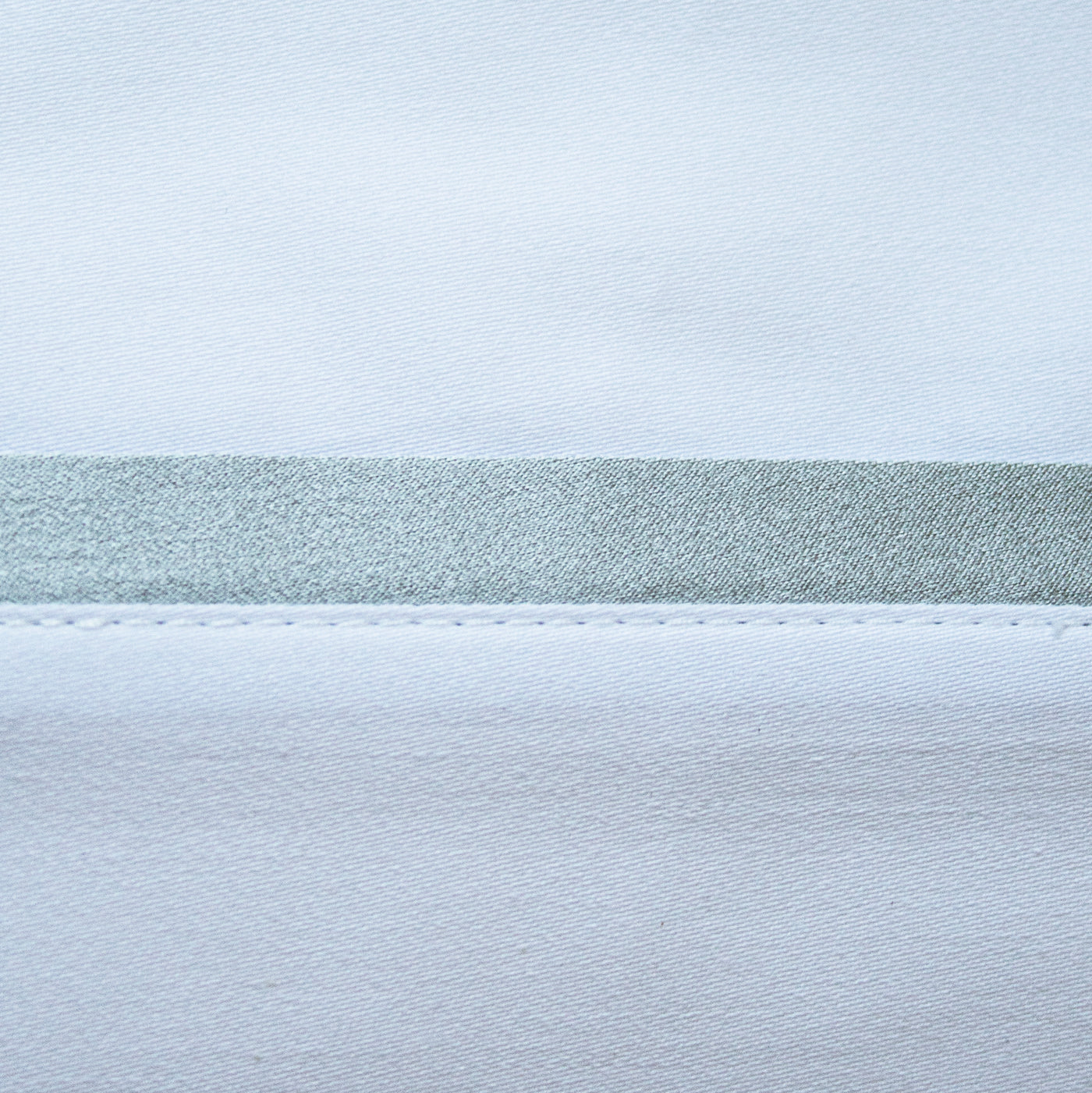 Close-up of pale blue silk pillowcase hem with sage green satin trim band.