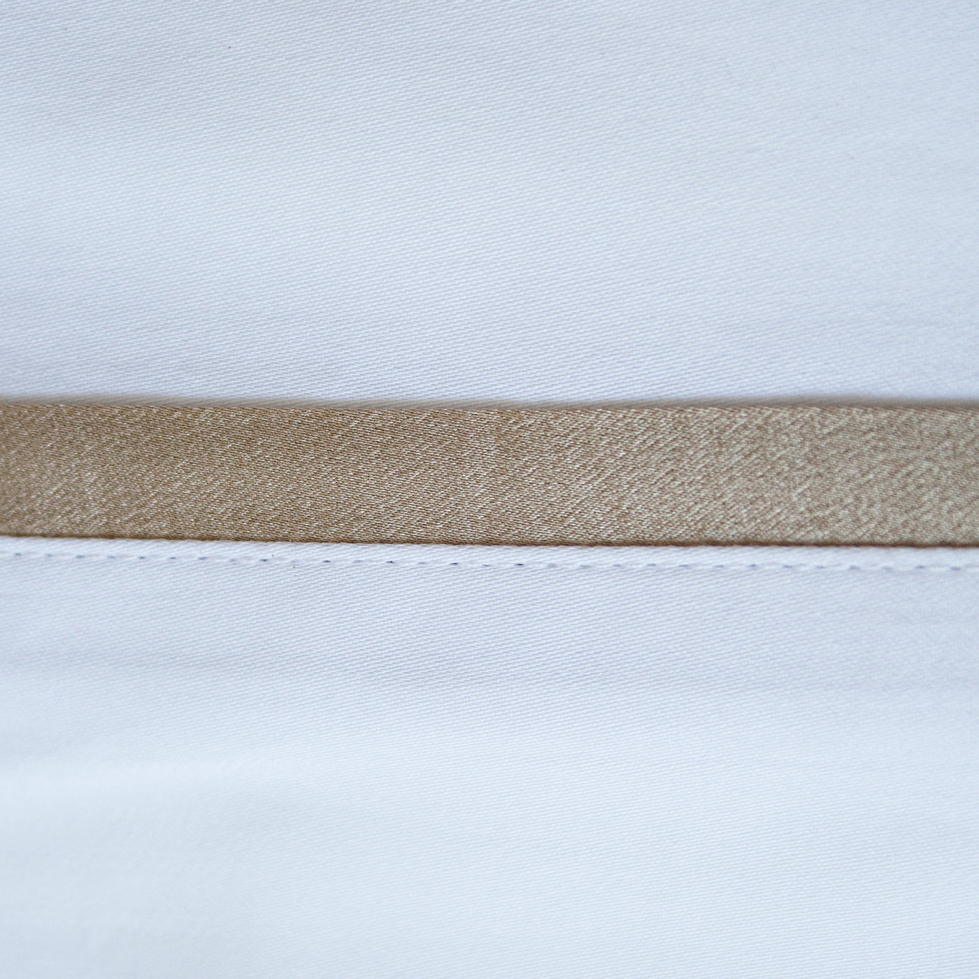 Close-up of champagne silk trim band on white pillowcase hem.