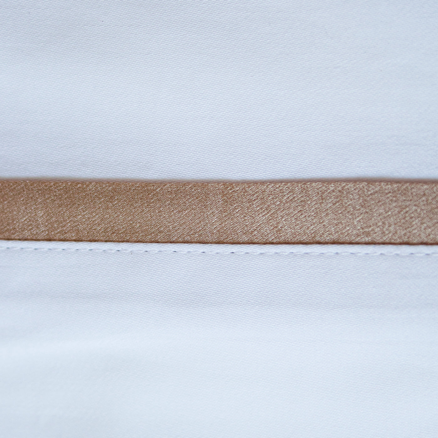 Close-up of champagne silk trim band on white Ann Gish pillowcase.