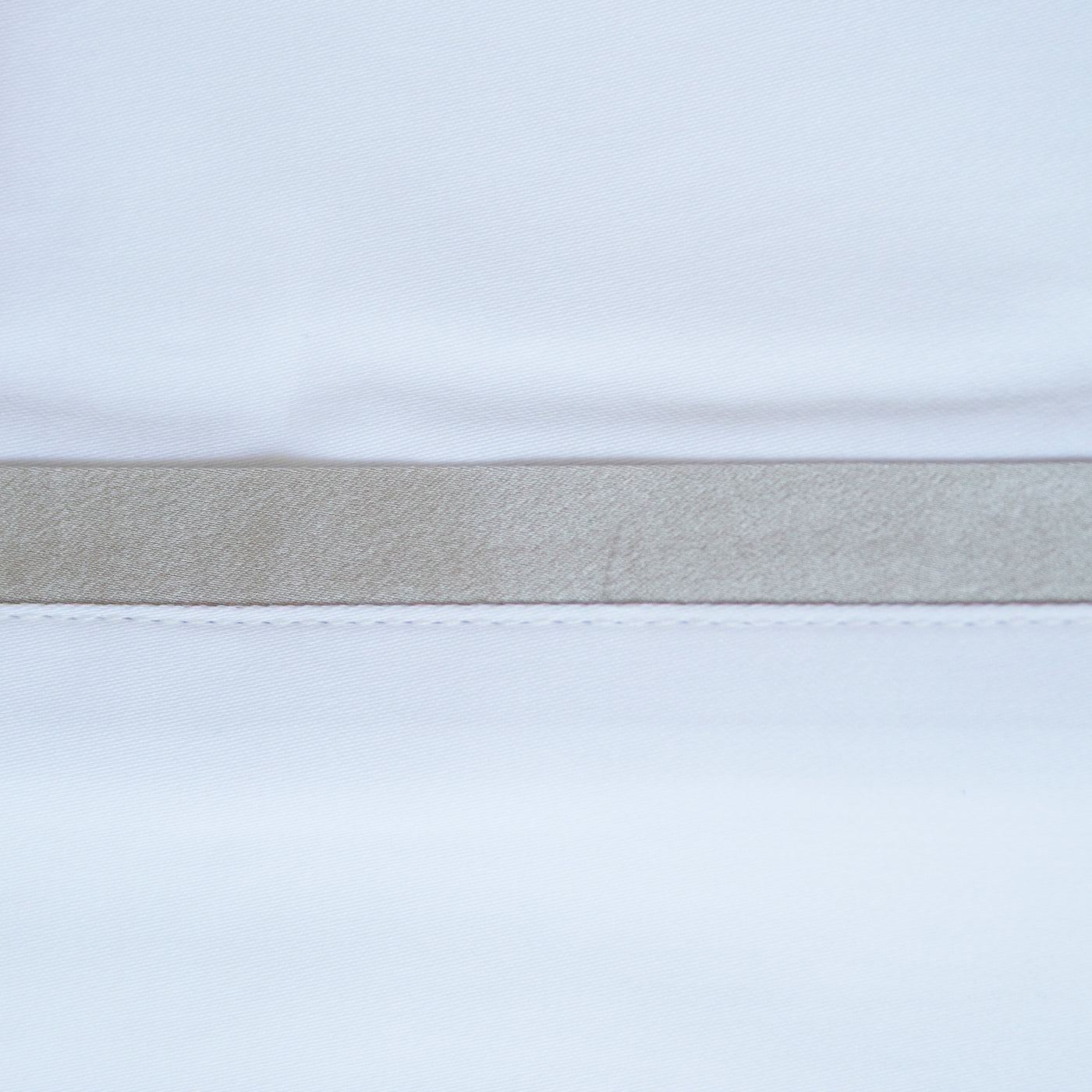 Close-up of white pillowcase hem with a wide taupe silk trim band and contrast stitching.
