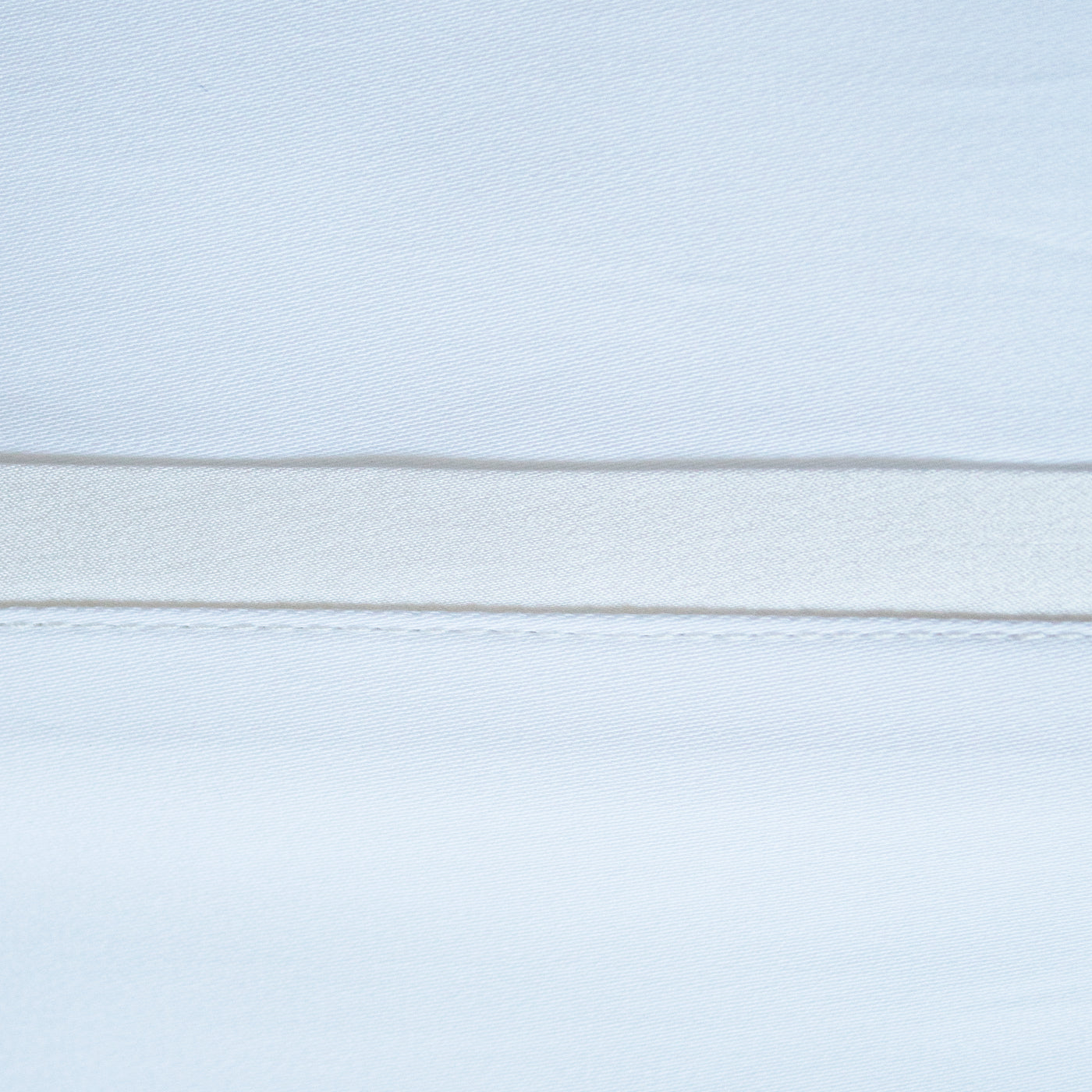 Close-up of pale blue pillowcase hem with ivory silk trim detail.